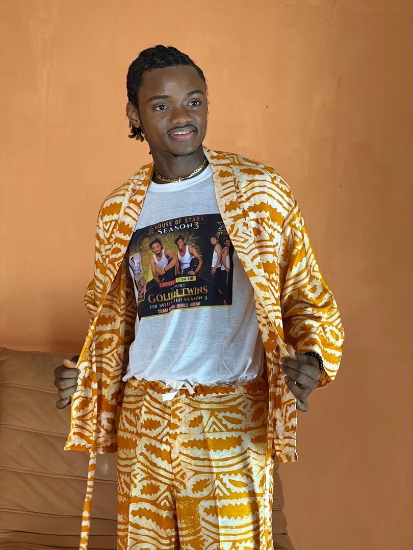 Jacob Sesay wearing the Golden Twins House of Stars Season 3 support shirt in traditional gold attire